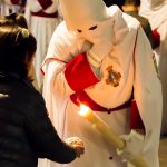 A penitent gives wax to a child in the crowd. The children make wax balls as the processions pass by, and compete with each other to have the largest.