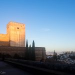 A picture of the Alhambra palace lit up with the dawn sunlight, with the houses of Granada in the background and a balloon making a dawn flight.