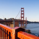 A picture of the Golden Gate Bridge with the red railing curving around in the foreground.