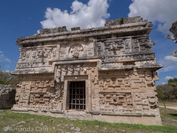 One of the richly decorated buildings in Chichen Itza. You can see faces on all the walls, the roof, and the side edges of the building.