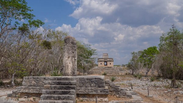A stela (carved slab) on a platform, and the Temple of the Seven Dolls in the background. On the equinoxes you can see the sun rise through the door of the temple.